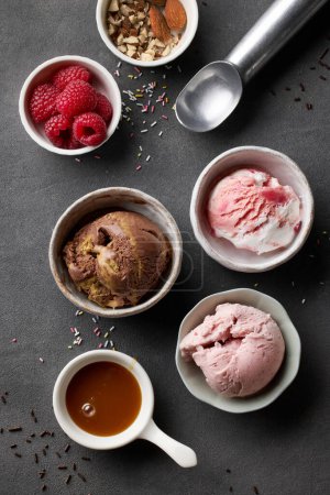 Téléchargez les photos : Bowls of various ice cream balls and serving ingredients on grey table, top view - en image libre de droit