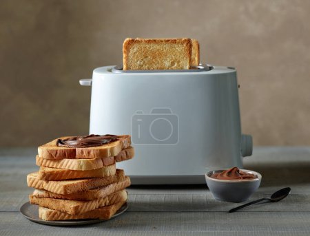 Foto de Heap of toasted bread slices and toaster on kitchen table - Imagen libre de derechos