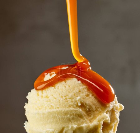 Foto de Salsa de caramelo que fluye en bola de helado de vainilla sobre fondo gris - Imagen libre de derechos