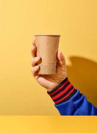 Foto de Quitar la taza de café en mano humana sobre fondo amarillo - Imagen libre de derechos