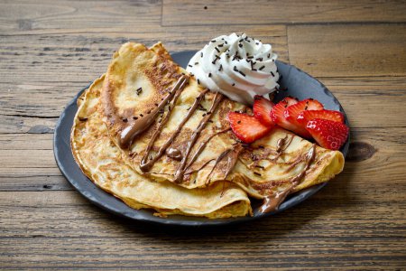 Téléchargez les photos : Assiette de crêpes décorées de crème fouettée et de fraises sur table en bois - en image libre de droit