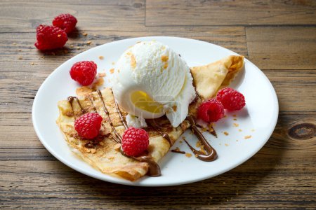 Foto de Crepe recién horneado con helado y frambuesas en mesa de madera - Imagen libre de derechos