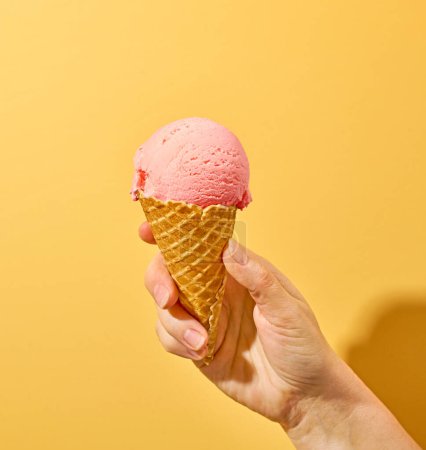 Téléchargez les photos : Crème glacée rose à la main humaine sur fond jaune - en image libre de droit
