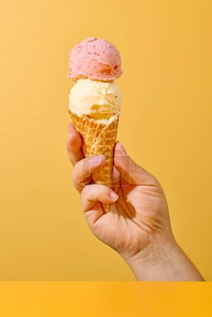 Foto de Ice cream in human hand on yellow background - Imagen libre de derechos