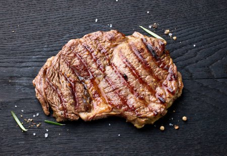 Foto de Carne de res recién asada entrecote filete en tablero de madera negro, vista superior - Imagen libre de derechos