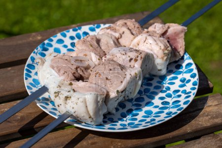 Foto de Plato de brochetas de cerdo marinadas crudas en mesa de picnic de madera - Imagen libre de derechos