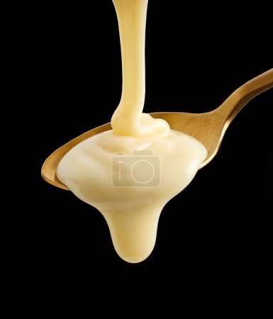 Téléchargez les photos : Verser du lait condensé dans une cuillère dorée isolée sur fond noir - en image libre de droit