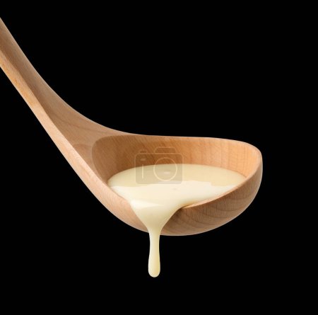 condensed milk in wooden ladle isolated on black background