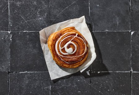 Photo for Freshly baked sweet cinnamon roll on dark grey scratched tiles background, top view - Royalty Free Image