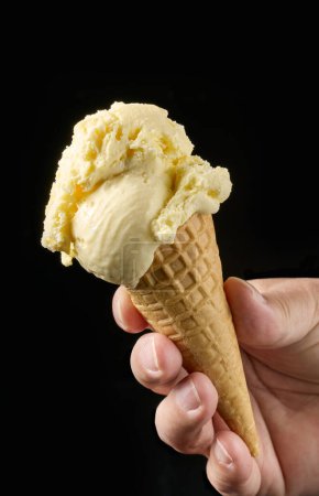 Photo for Close up of vanilla ice cream in waffle cone in human hand isolated on black background - Royalty Free Image