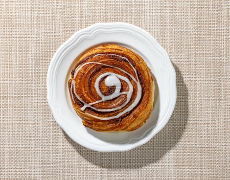 Photo for Freshly baked sweet cinnamon roll on white plate, top view - Royalty Free Image