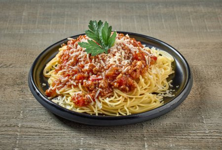 Photo for Spaghetti with sauce bolognese on black plate on wooden kitchen table - Royalty Free Image