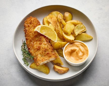 Téléchargez les photos : Un bol de fish and chips. Filet de poisson pané avec coins de pommes de terre frites sur table de cuisine gris clair, vue sur le dessus - en image libre de droit