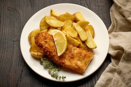 Téléchargez les photos : Assiette de fish and chips, filet de poisson pané et quartiers de pommes de terre frites sur table en bois foncé, vue de dessus - en image libre de droit