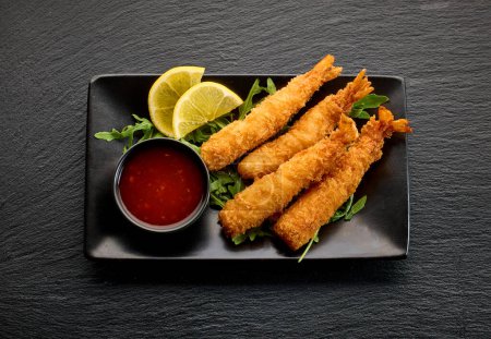 Photo for Plate of breaded Torpedo shrimps on black tile background, top view - Royalty Free Image