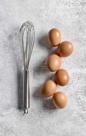 Photo for Brown eggs and whisk on light grey painted kitchen table background, top view - Royalty Free Image