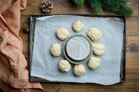 Foto de Bollos de masa de levadura cruda y queso brie en la bandeja para hornear, vista superior. Fondo para hornear Navidad - Imagen libre de derechos