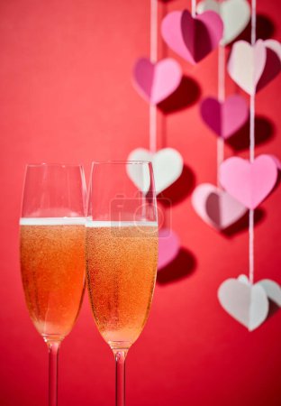 Photo for Two glasses of champagne and defocused heart shaped decoration on red background - Royalty Free Image