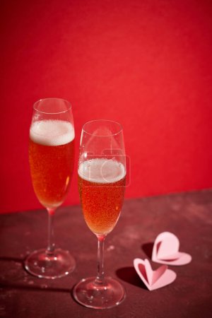 Photo for Two glasses of champagne and heart shaped decorations on red background - Royalty Free Image
