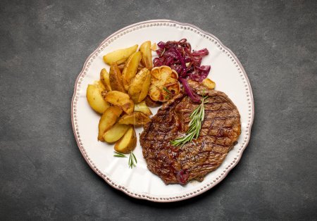 Photo for Plate of freshly grilled steak and fried potatoes on dark grey background, top view - Royalty Free Image