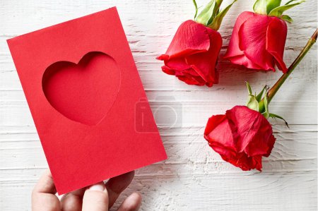 Photo for Red roses and heart shaped greeting card on white wooden background, top view - Royalty Free Image