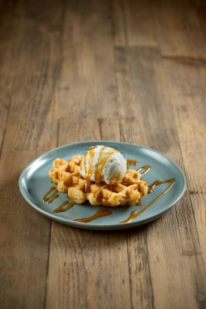 Photo for Plate of belgian waffle decorated with caramel sauce and vanilla ice cream scoop on wooden table - Royalty Free Image