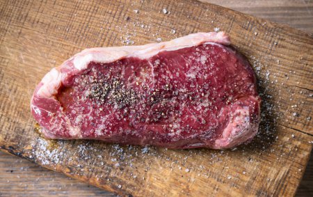 Photo for Fresh raw beef steak meat with salt and pepper on wooden cutting board, top view - Royalty Free Image