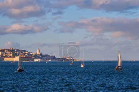 Téléchargez les photos : Vue de Lisbonne sur le Tage depuis Almada avec des yachts bateaux de tourisme au coucher du soleil avec un ciel spectaculaire. Lisbonne, Portugal - en image libre de droit