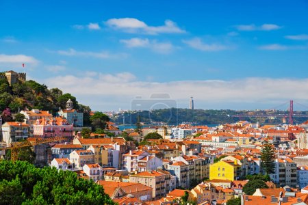 Photo for Lisbon famous view from Miradouro dos Barros tourist viewpoint over Alfama old city district with St. Georges Castle and Portugal flag, 25th of April Bridge, Christ the King statue. Lisbon, Portugal. - Royalty Free Image