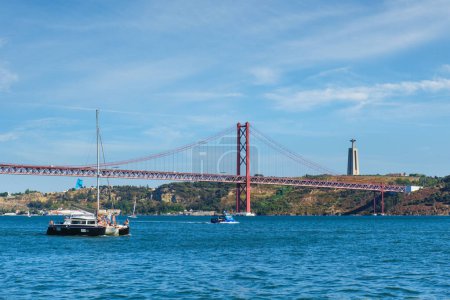 Foto de Vista del Puente 25 de Abril famoso monumento turístico sobre el río Tajo, el monumento a Cristo Rey y un yate turístico. Lisboa, Portugal - Imagen libre de derechos
