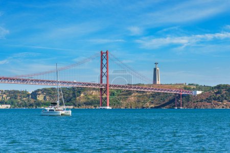 Foto de Vista del Puente 25 de Abril famoso monumento turístico sobre el río Tajo, el monumento a Cristo Rey y un yate turístico. Lisboa, Portugal - Imagen libre de derechos