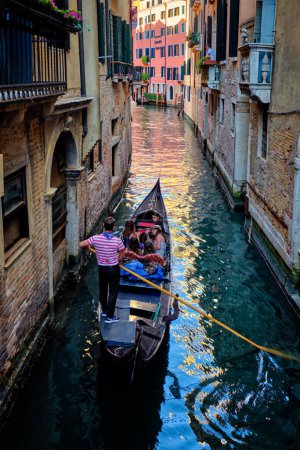 Foto de VENECIA, ITALIA - 27 DE JUNIO DE 2018: Estrecho canal entre coloridas casas antiguas con góndola barco con turistas y gonolier en Venecia, Italia - Imagen libre de derechos