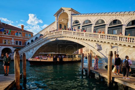 Téléchargez les photos : VENISE, ITALIE - 27 JUIN 2018 : Pont du Rialto avec vaporetto passant sous le Grand Canal au coucher du soleil, Venise, Italie - en image libre de droit