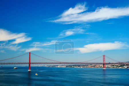 Foto de Vista del puente 25 de Abril famoso monumento turístico de Lisboa que conecta Lisboa con Almada en la península de Setúbal sobre el río Tajo con barcos yates, barcos y avión volador. Lisboa, Portugal - Imagen libre de derechos