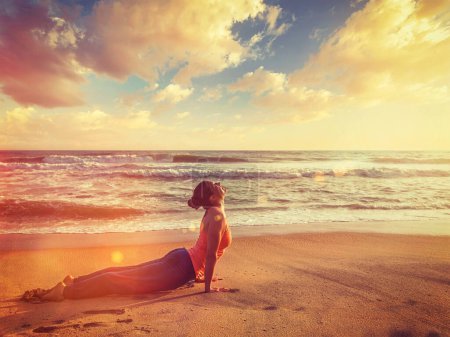 Téléchargez les photos : Yoga en plein air sur la plage - la femme pratique Ashtanga Vinyasa yoga Surya Namaskar Soleil Salutation asana Urdhva Mukha Svanasana - pose de chien vers le haut sur le coucher du soleil. Avec fuite de lumière et éclat de lentille - en image libre de droit