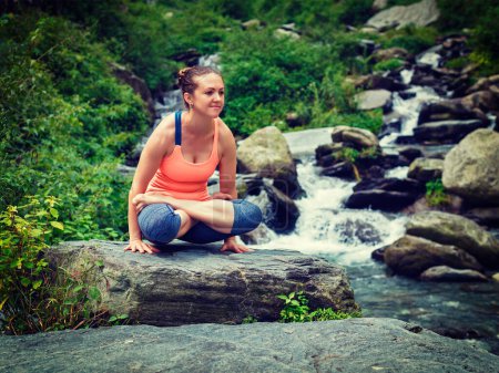 Téléchargez les photos : Exercice de yoga en plein air - femme faisant Ashtanga Vinyasa Yoga bras équilibre musculation asana Tolasana - échelles posent à la cascade en Himalaya. Vintage effet rétro filtré image de style hipster - en image libre de droit