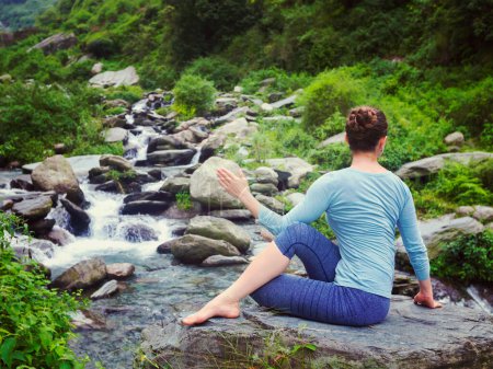 Photo for Yoga exercise outdoors - woman doing Ardha matsyendrasana asana - half spinal twist pose at tropical waterfall in Himalayas in India. Vintage retro effect filtered hipster style image. - Royalty Free Image