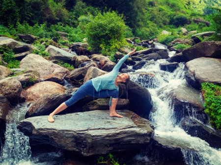 Photo for Sporty fit woman practices yoga asana Utthita Parsvakonasana - extended side angle pose outdoors at water. Vintage retro effect filtered hipster style image. - Royalty Free Image