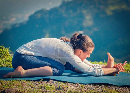 Téléchargez les photos : Yoga en plein air femme faisant Ashtanga Vinyasa yoga Tiryam-Mukha Eka-Pada Paschimottanasana asana position d'étirement en plein air. Vintage effet rétro filtré image de style hipster. - en image libre de droit