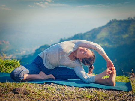 Photo for Yoga outdoors - young sporty fit woman doing Hatha Yoga asana parivritta janu sirsasana - Revolved Head-to-Knee Pose - in mountains in the morning. Vintage retro effect filtered hipster style image. - Royalty Free Image