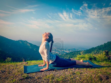 Foto de Yoga al aire libre - mujer practica Ashtanga Vinyasa yoga Surya Namaskar Sun Salutation asana Urdhva Mukha Svanasana hacia arriba posando de perro en las montañas por la mañana. Vintage efecto retro imagen filtrada - Imagen libre de derechos