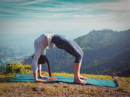 Téléchargez les photos : Yoga en plein air femme faisant Ashtanga Vinyasa Yoga asana Urdhva Dhanurasana pose d'arc vers le haut dans les montagnes de l'Himalaya le matin Himachal Pradesh, Inde. Vintage effet rétro filtré image - en image libre de droit