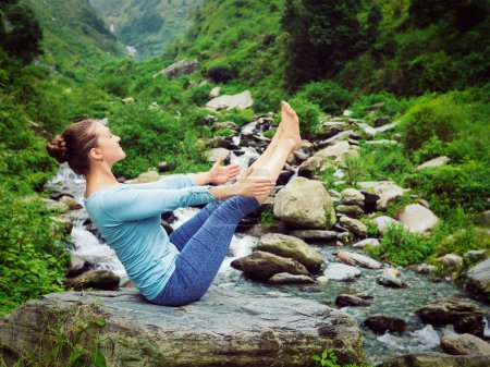 Photo for Yoga outdoors - woman doing Ashtanga Vinyasa Yoga asana Navasana - boat pose - in Himalayas at tropical waterfall. Himachal Pradesh, India. Vintage retro effect filtered hipster style image - Royalty Free Image