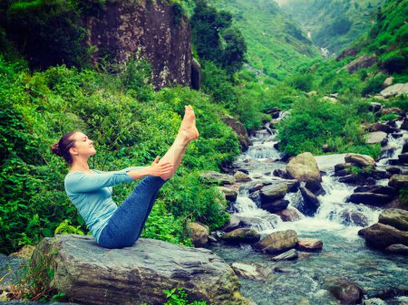 Photo for Yoga outdoors - woman doing Ashtanga Vinyasa Yoga asana Navasana - boat pose - in Himalayas at tropical waterfall. Himachal Pradesh, India. Vintage retro effect filtered hipster style image - Royalty Free Image