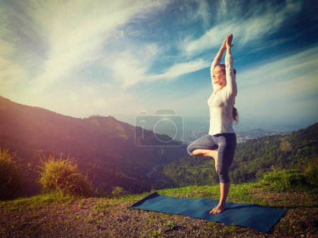 Yoga Praxis im Freien - Frau übt Balance Yoga Asana Vrikshasana Baum Pose im Himalaya Berge im Freien in der Früh. Himachal Pradesh, Indien. Panorama. Vintage Retro-Effekt gefiltertes Bild