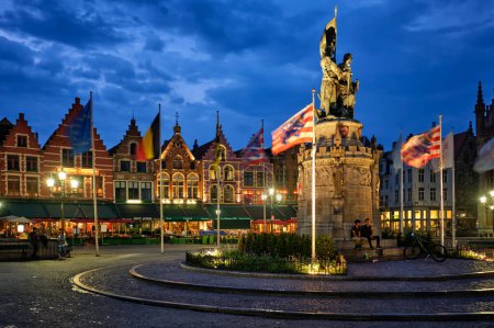 Foto de Brujas, Bélgica - 29 de mayo de 2018: Brujas Grote plaza del mercado famoso lugar turístico con muchos cafés y restaurantes y Jan Breydel y Pieter de Coninck Monumento por la noche - Imagen libre de derechos