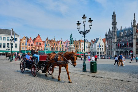 Foto de Brujas, Bélgica - 29 de mayo de 2018: Carro de caballos para los turistas en Brujas Grote plaza del mercado famoso lugar turístico con muchos cafés y restaurantes - Imagen libre de derechos