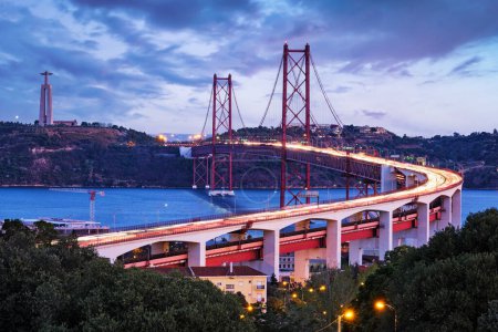Photo for View of Lisbon view from Miradouro do Bairro do Alvito viewpoint of Tagus river, traffic with light trails on 25th of April Bridge, and Christ the King statue in the evening twilight. Lisbon, Portugal - Royalty Free Image