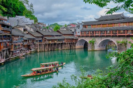 Photo for FENGHUANG, CHINA - APRIL 23, 2018: Chinese tourist attraction destination - Feng Huang Ancient Town (Phoenix Ancient Town) on Tuo Jiang River with bridge and tourist boat. Hunan Province, China - Royalty Free Image