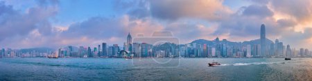 Téléchargez les photos : HONG KONG, CHINE - 28 AVRIL 2018 : Panorama des gratte-ciels du centre-ville de Hong Kong au-dessus du port de Victoria le soir au coucher du soleil avec des ferries pour bateaux touristiques. Hong Kong, Chine - en image libre de droit